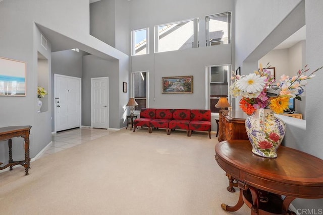 interior space with a towering ceiling, light tile patterned floors, visible vents, and light colored carpet