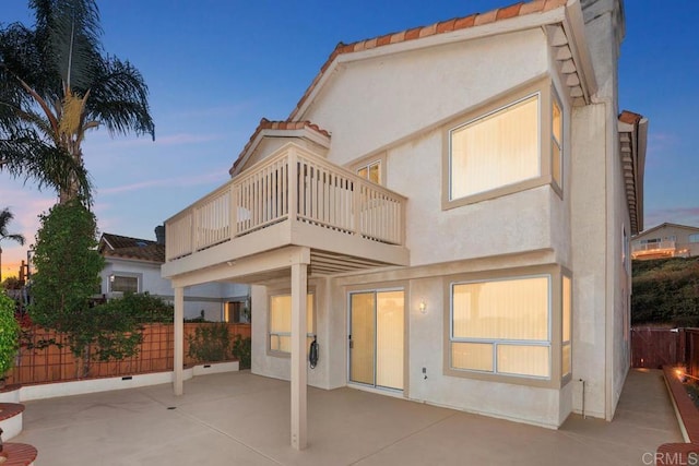 back of house featuring a patio, a balcony, a tiled roof, fence, and stucco siding