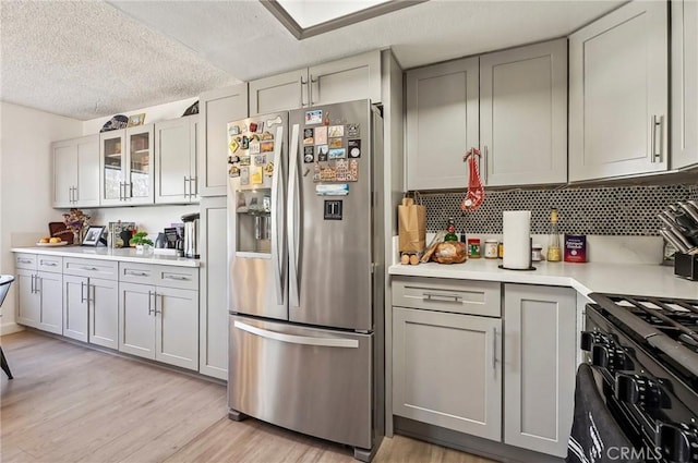 kitchen with black gas range oven, stainless steel fridge, backsplash, a textured ceiling, and light hardwood / wood-style flooring