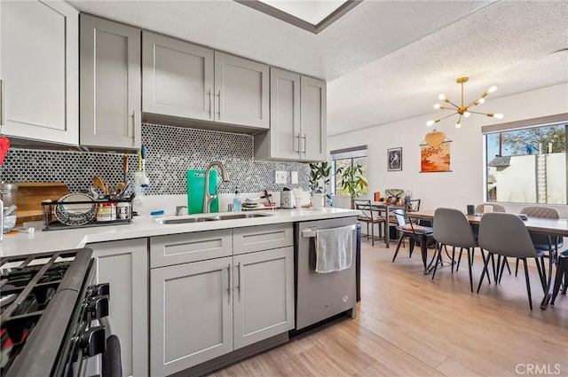 kitchen with gray cabinets, range with gas stovetop, sink, stainless steel dishwasher, and plenty of natural light