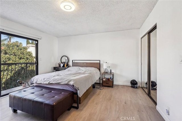 bedroom with a closet, access to outside, a textured ceiling, and light hardwood / wood-style flooring