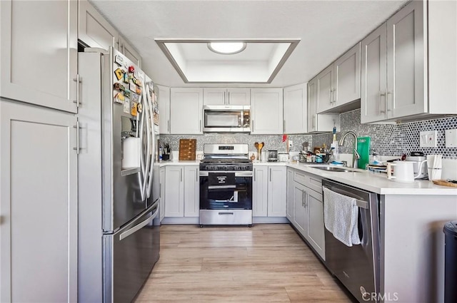 kitchen featuring appliances with stainless steel finishes, sink, decorative backsplash, a raised ceiling, and light wood-type flooring