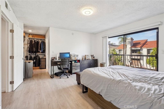 bedroom featuring a walk in closet, access to exterior, a textured ceiling, and light wood-type flooring