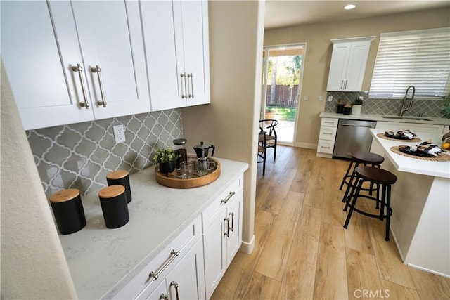 kitchen with sink, white cabinets, backsplash, stainless steel dishwasher, and light hardwood / wood-style flooring