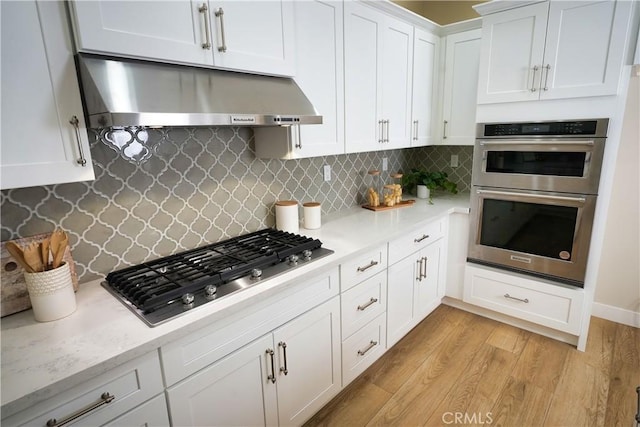 kitchen featuring light hardwood / wood-style flooring, appliances with stainless steel finishes, light stone counters, white cabinets, and decorative backsplash