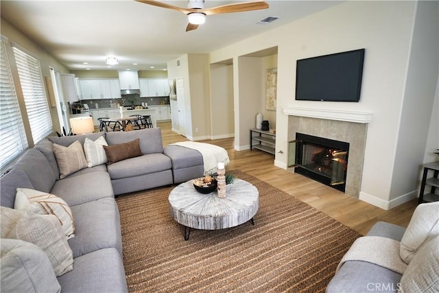 living room featuring ceiling fan, a fireplace, and light wood-type flooring