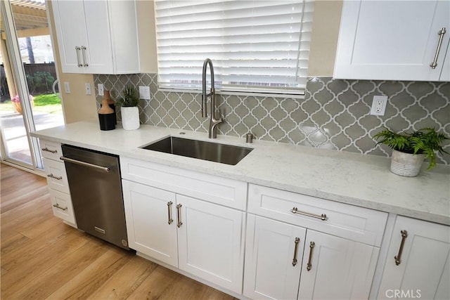 kitchen with sink, white cabinetry, light stone counters, stainless steel dishwasher, and light wood-type flooring