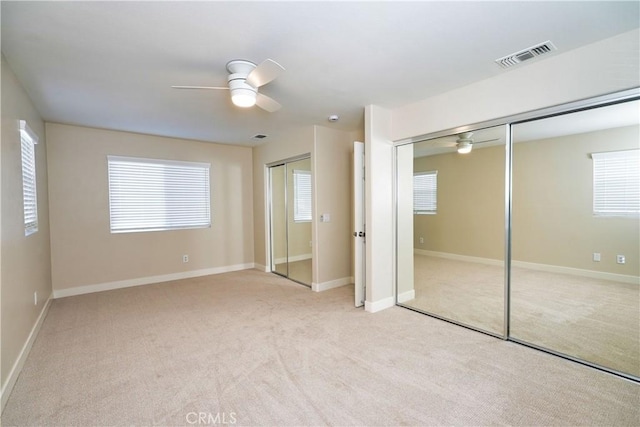 unfurnished bedroom with multiple closets, light carpet, and ceiling fan