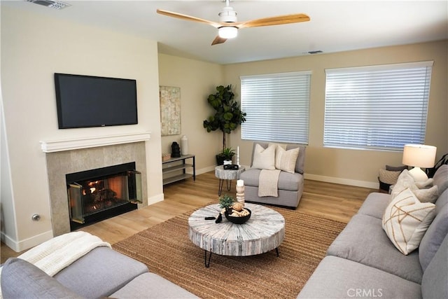 living room featuring a tile fireplace, ceiling fan, and light wood-type flooring