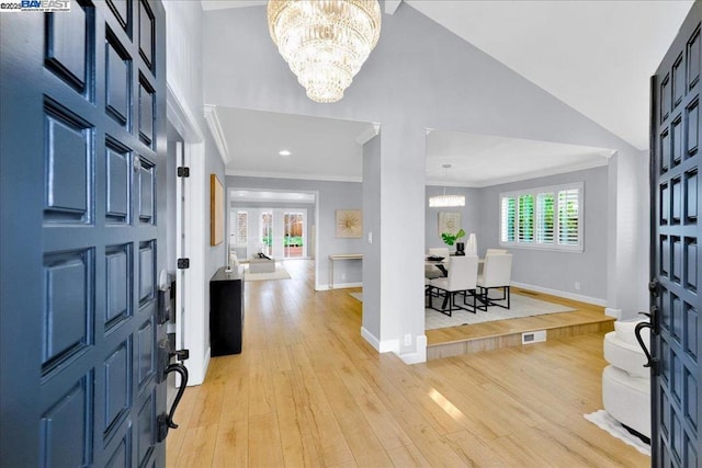 entrance foyer featuring ornamental molding, high vaulted ceiling, a chandelier, and light hardwood / wood-style flooring