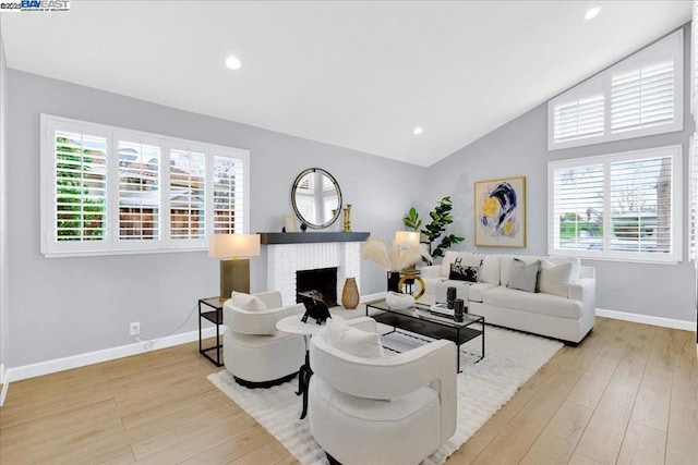 living room featuring a brick fireplace, lofted ceiling, and light hardwood / wood-style floors