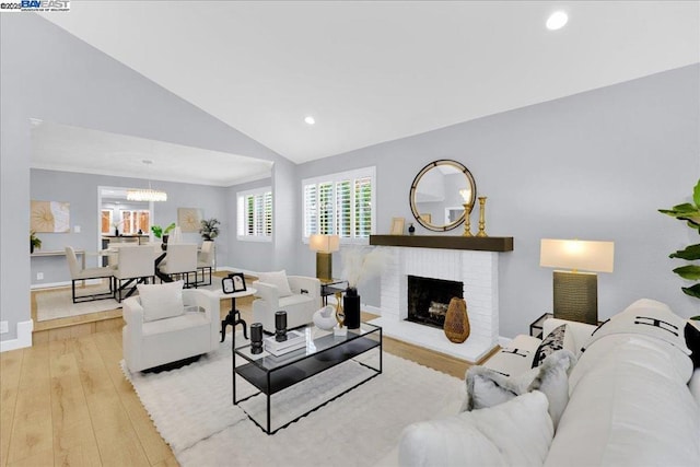 living room with a notable chandelier, vaulted ceiling, a fireplace, and light wood-type flooring