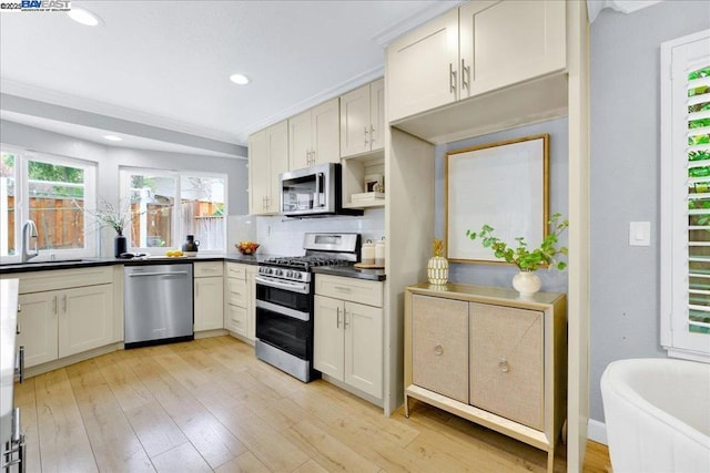 kitchen with appliances with stainless steel finishes, sink, light wood-type flooring, and decorative backsplash