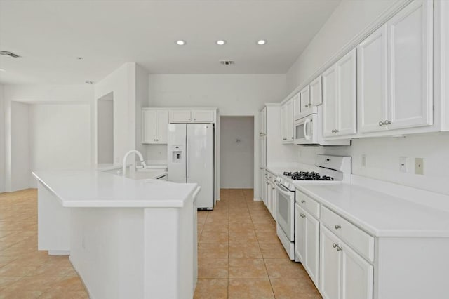 kitchen featuring sink, light tile patterned floors, an island with sink, white appliances, and white cabinets