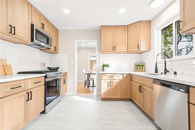 kitchen featuring light countertops, appliances with stainless steel finishes, a sink, and light brown cabinetry