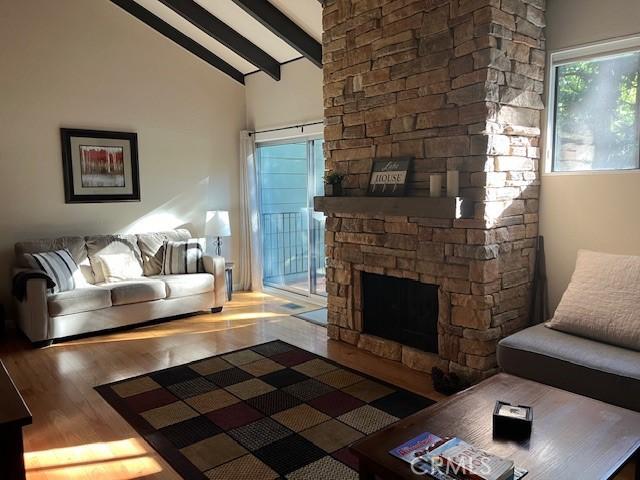 living room with beam ceiling, a stone fireplace, hardwood / wood-style flooring, and high vaulted ceiling