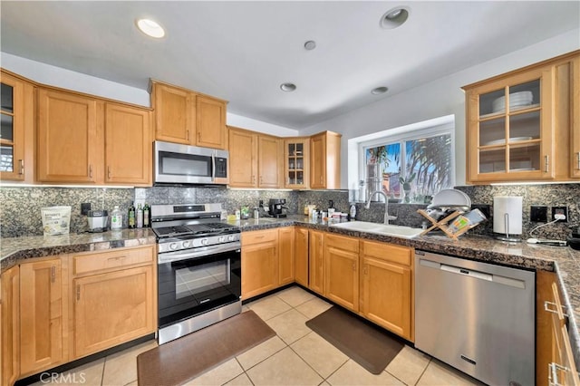 kitchen featuring sink, light tile patterned floors, appliances with stainless steel finishes, dark stone countertops, and backsplash