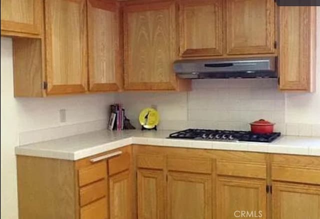 kitchen featuring stainless steel gas stovetop, tile countertops, and backsplash