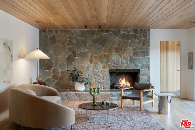 living room with wood ceiling, a stone fireplace, and hardwood / wood-style flooring