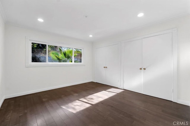 unfurnished bedroom featuring two closets and dark wood-type flooring