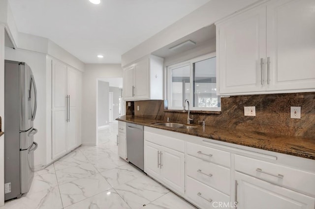 kitchen featuring sink, white cabinetry, dark stone counters, stainless steel appliances, and backsplash