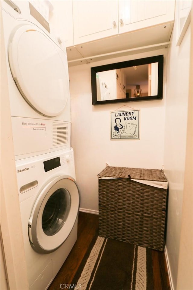 laundry area featuring dark wood-type flooring, cabinets, and stacked washer / dryer