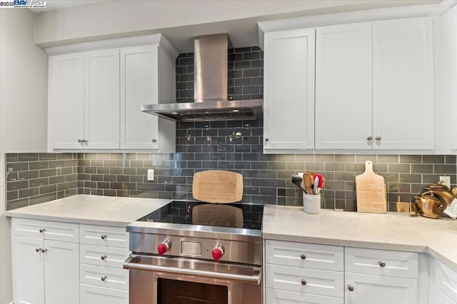 kitchen with backsplash, white cabinets, high end range, and wall chimney range hood