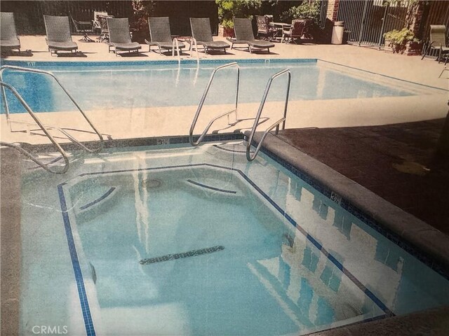 view of swimming pool with fence, a community hot tub, and a patio area