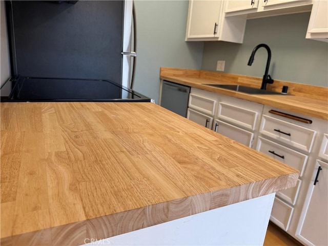 kitchen with butcher block countertops, a sink, stainless steel dishwasher, white cabinetry, and fridge