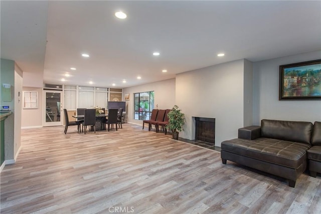 living area featuring a fireplace with flush hearth, recessed lighting, baseboards, and light wood-style floors