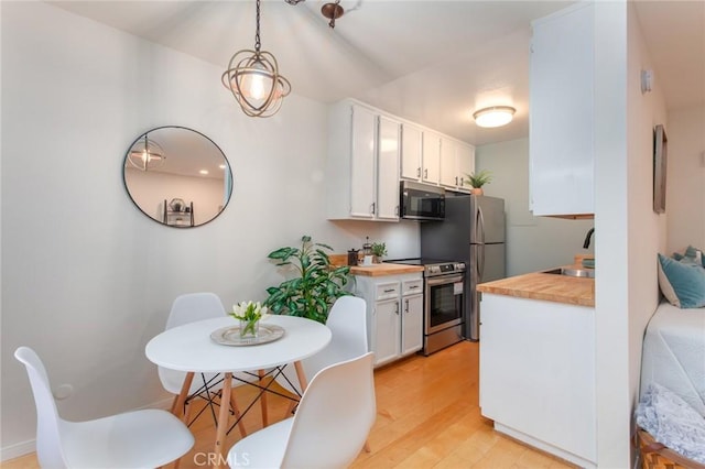 kitchen with appliances with stainless steel finishes, sink, white cabinets, hanging light fixtures, and light hardwood / wood-style flooring