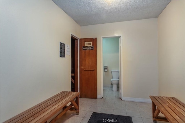 hall with light tile patterned flooring, baseboards, and a textured ceiling