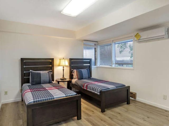bedroom featuring baseboards, wood finished floors, and a wall unit AC