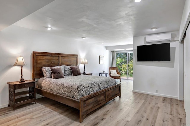 bedroom featuring a wall mounted AC, light wood-style flooring, and baseboards
