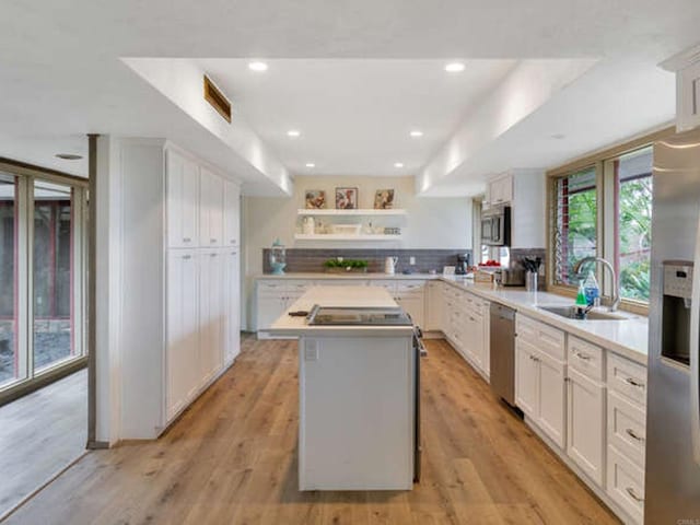 kitchen featuring white cabinets, light countertops, a sink, a kitchen island, and appliances with stainless steel finishes