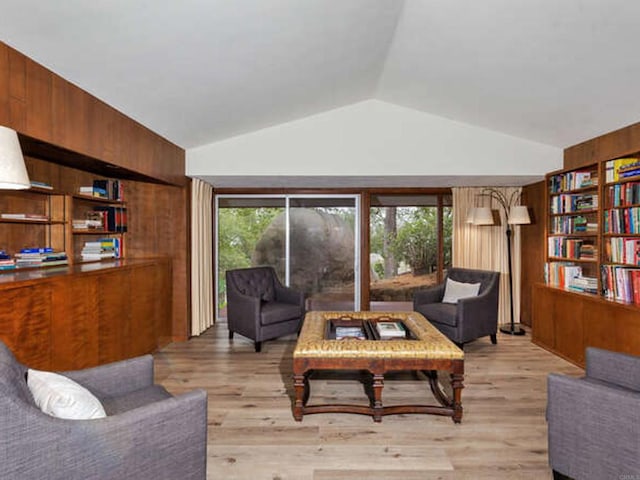 living area with wooden walls, vaulted ceiling, and light wood-style floors