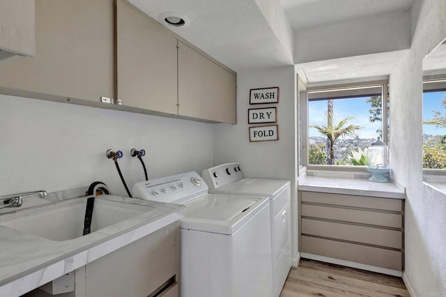 washroom with cabinet space, light wood-type flooring, washing machine and clothes dryer, and a sink
