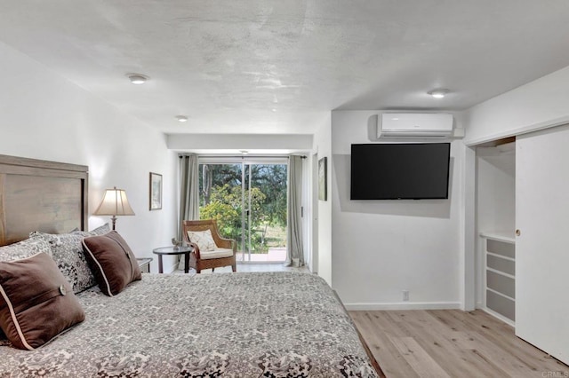 bedroom with baseboards, light wood-style floors, a wall mounted AC, and access to exterior