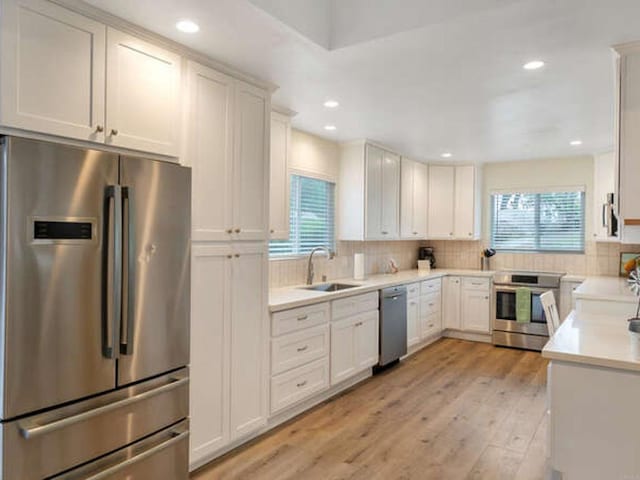 kitchen with light wood finished floors, stainless steel appliances, light countertops, a sink, and tasteful backsplash