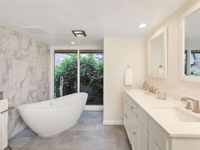 full bathroom featuring a soaking tub, a sink, double vanity, and recessed lighting