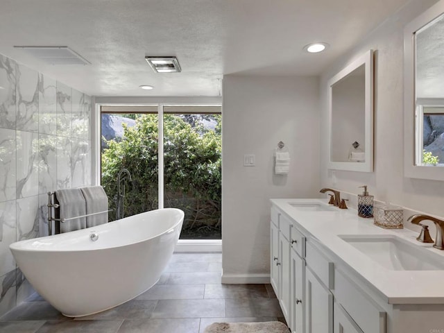 full bathroom with double vanity, visible vents, a sink, and a freestanding bath