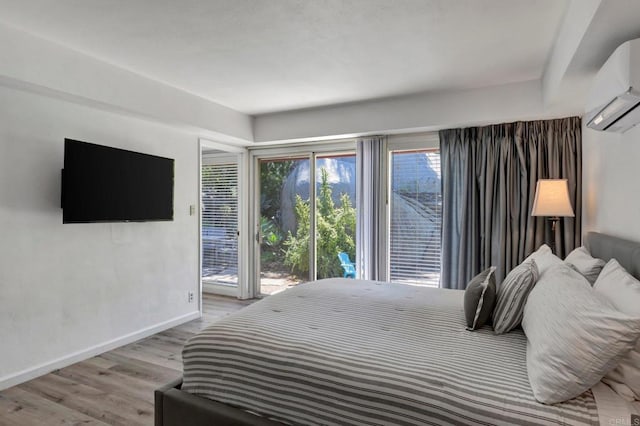bedroom featuring a wall mounted AC, light wood-style floors, baseboards, and access to exterior