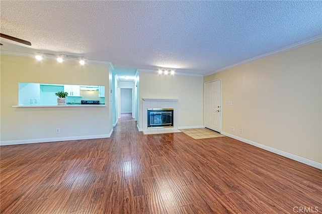 unfurnished living room featuring a tile fireplace, wood-type flooring, a textured ceiling, and crown molding