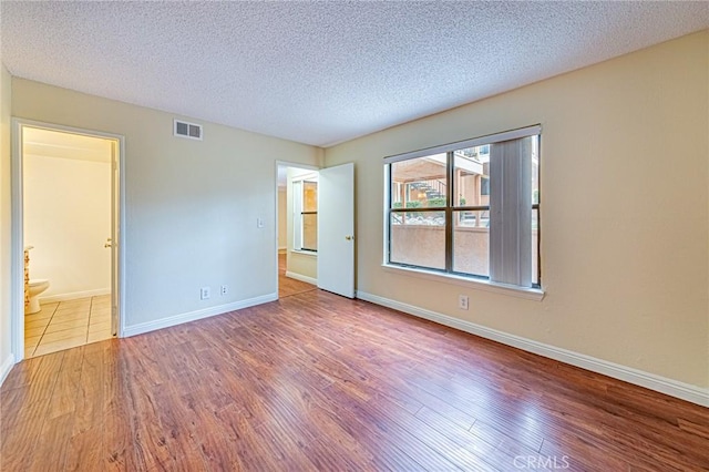 unfurnished bedroom featuring hardwood / wood-style flooring, ensuite bath, and a textured ceiling