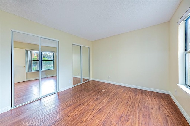 unfurnished bedroom with hardwood / wood-style floors, a textured ceiling, and multiple closets