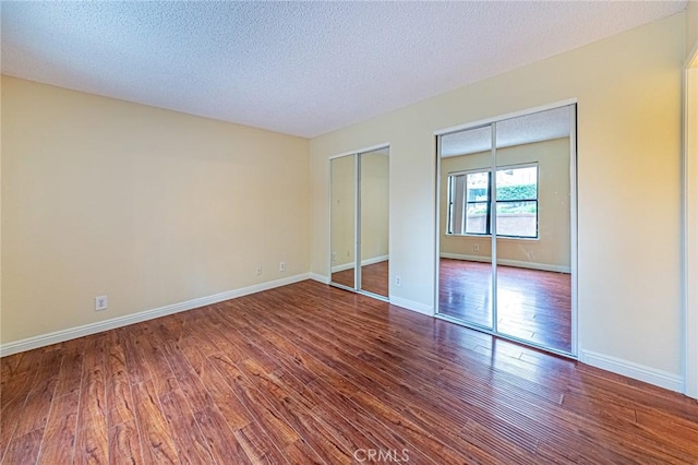 unfurnished bedroom featuring two closets, a textured ceiling, and hardwood / wood-style flooring