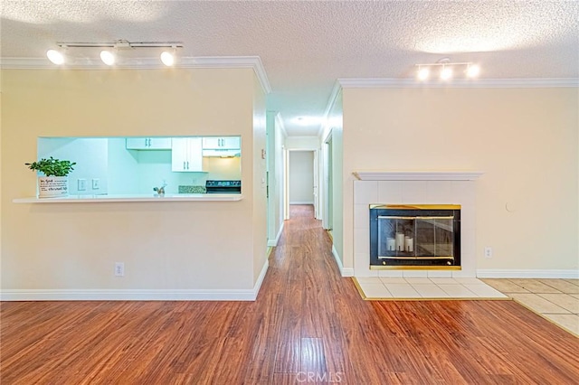 unfurnished living room with crown molding, hardwood / wood-style flooring, a tile fireplace, rail lighting, and a textured ceiling