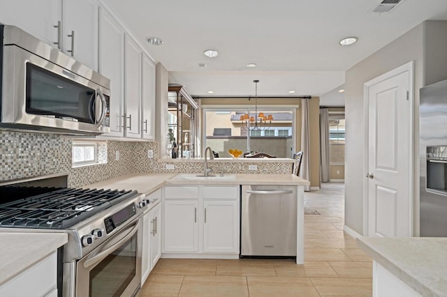 kitchen with appliances with stainless steel finishes, tasteful backsplash, sink, white cabinets, and hanging light fixtures