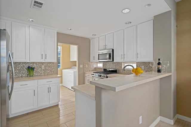 kitchen featuring sink, kitchen peninsula, stainless steel appliances, washer / clothes dryer, and white cabinets