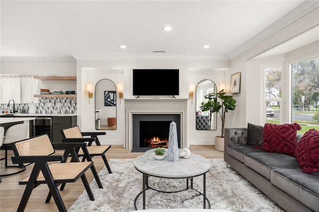 living room with wine cooler, sink, crown molding, and light wood-type flooring